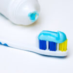A toothbrush has a streak of blue toothpaste on it next to a toothpaste tube on a white counter
