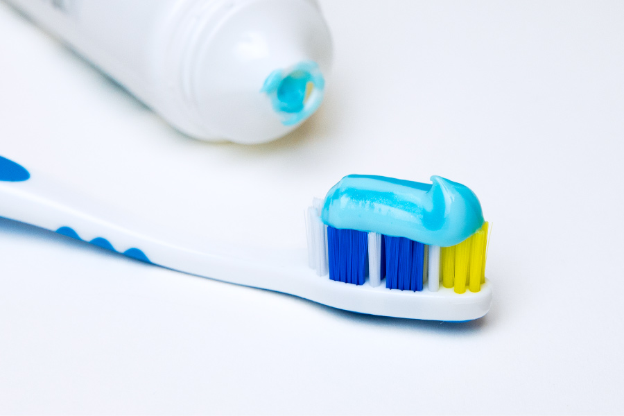 A toothbrush has a streak of blue toothpaste on it next to a toothpaste tube on a white counter